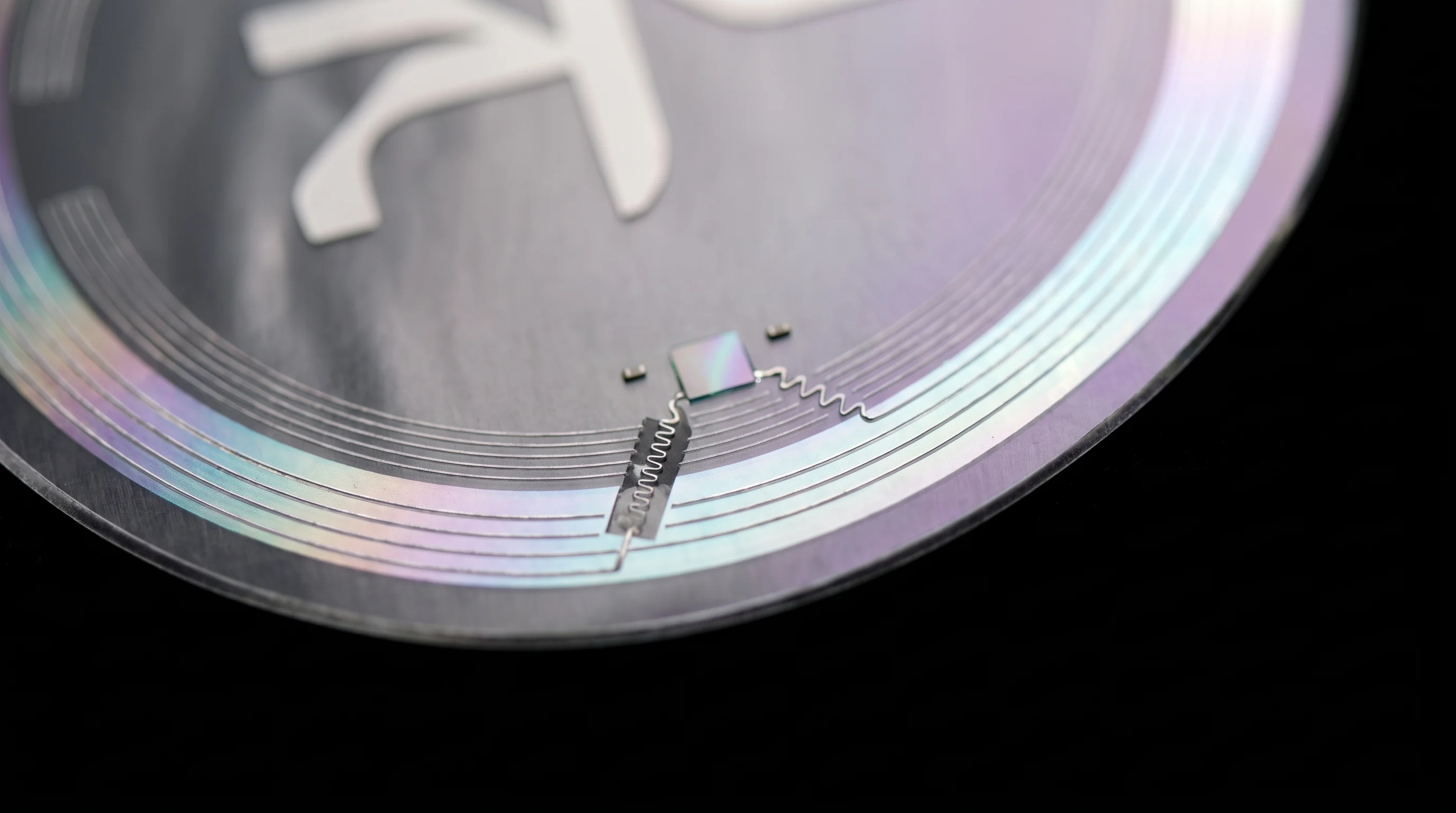 Macro of the Wave X.3: a round transparent silk film with a fine silver antenna near its rim, shimmering lilac and aqua.